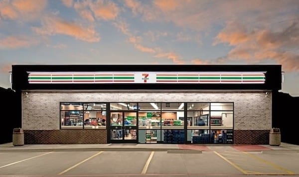 Exterior of a 7-eleven store in White Plains MD at dusk, with a colorful sunset sky in the background and lights illuminating the storefront.