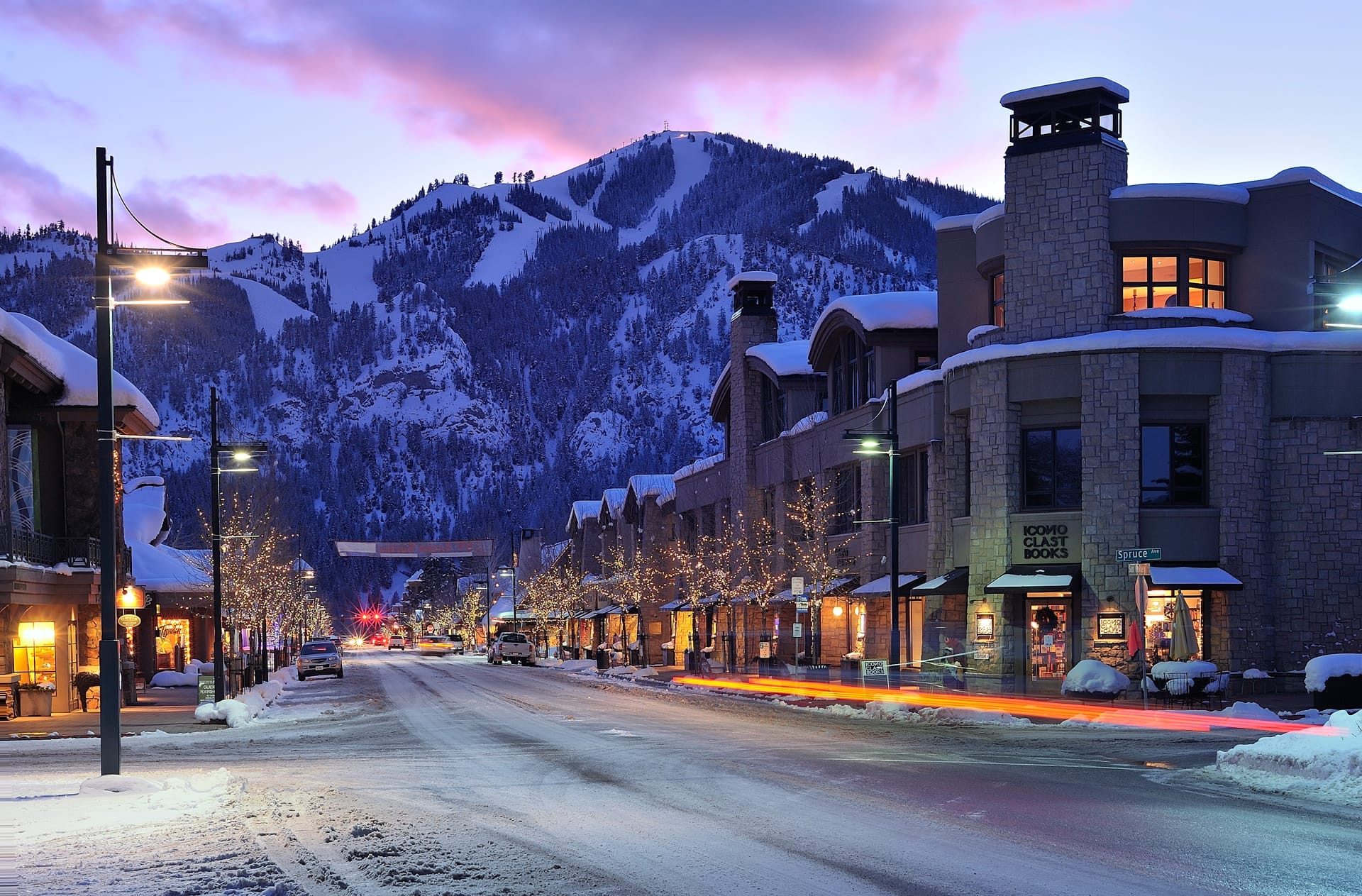 Sunset view of Sun Valley, Idaho, with snow-covered mountains in the background and lit-up street and buildings in the foreground, featuring the Thomas Company logo and announcement text about their relocation to Sun Valley