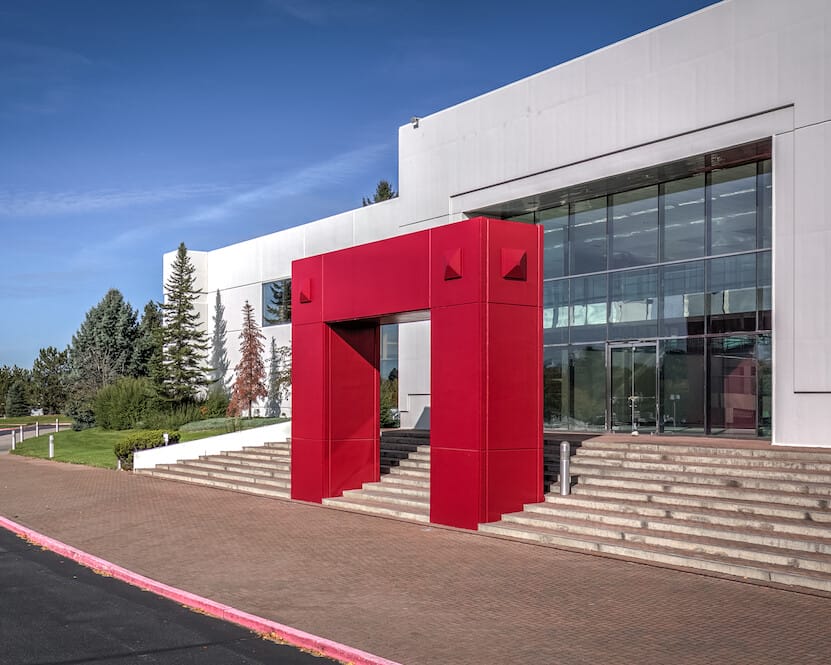 A modern distribution building with a large red geometric entrance, surrounded by a landscaped area under a clear blue sky.