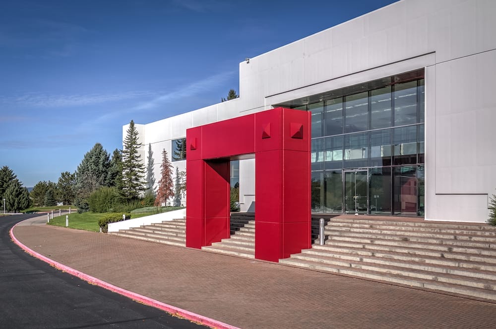 A modern distribution building with a large red geometric entrance, surrounded by a landscaped area under a clear blue sky.