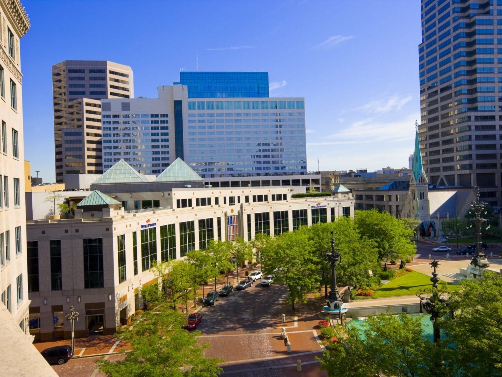 A sunny view of an urban downtown area featuring modern buildings, a lush green park, and a clear blue sky, ideal for asset sales.