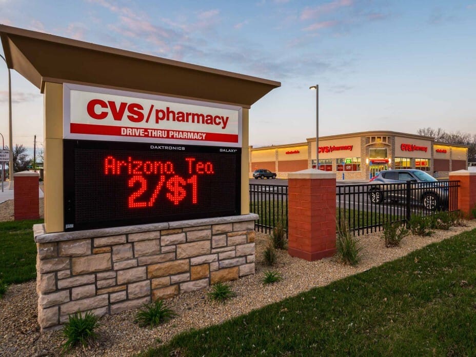A CVS Pharmacy branch at dusk, featuring a prominent electronic sign advertising a deal on Arizona tea, with the store illuminated in the background, catering to its multi-market portfolios.