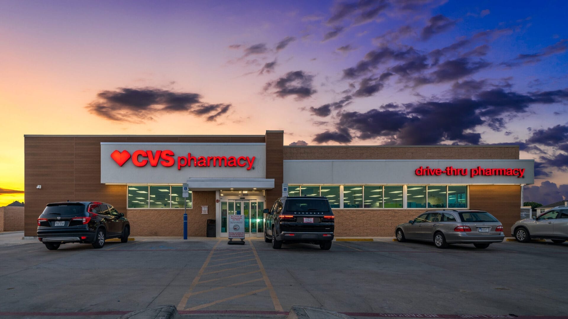 Exterior view of a recently sold CVS Pharmacy store in Fort Worth, Texas, during sunset with parked cars and a vibrant sky.