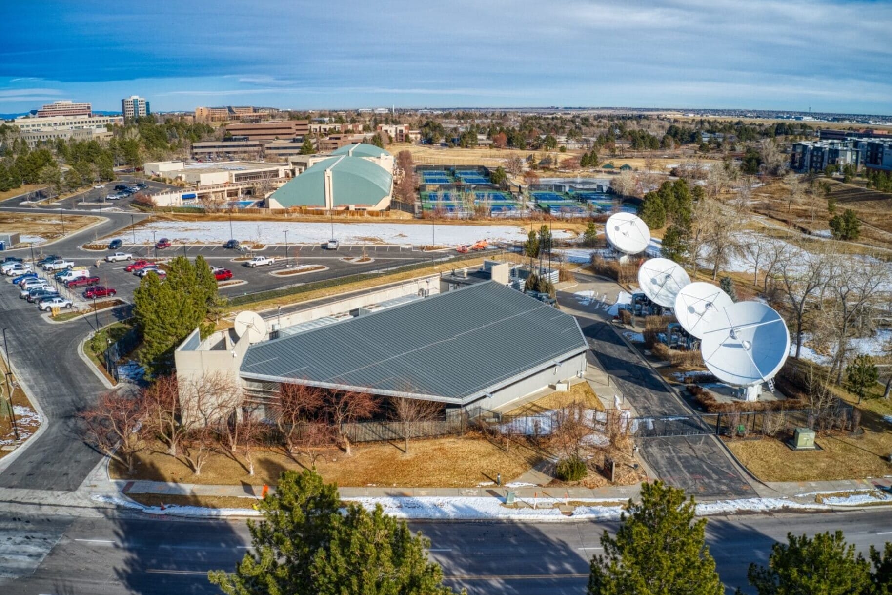 Aerial view of the DIRECTV Data Center Portfolio with buildings, satellite dishes, and a parking area, partially covered in snow.