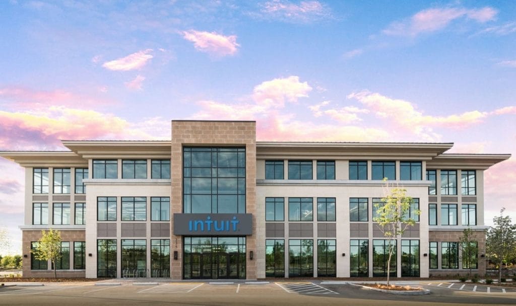 A modern three-story Intuit office building, specializing in financial software, with large windows and a clear sky background.