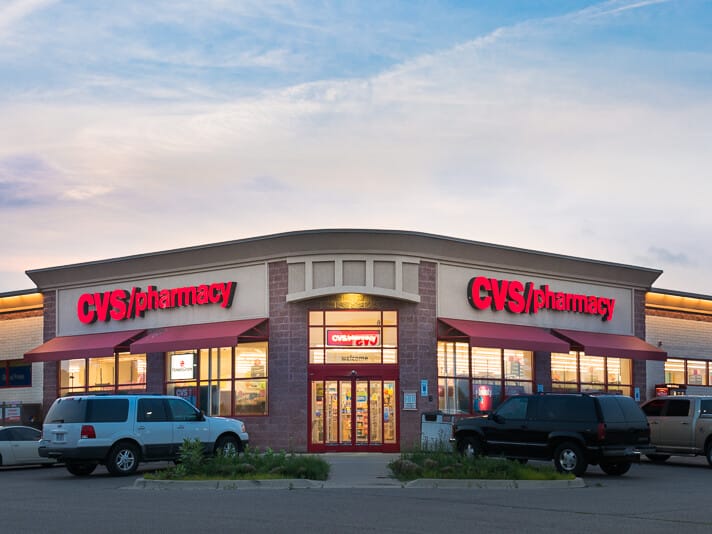 Exterior view of a CVS pharmacy store at dusk with illuminated signage and parked cars in the foreground, showcasing its presence in an unlevered portfolio.