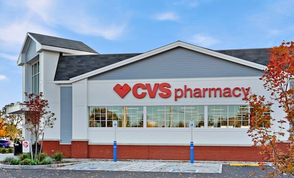 Exterior view of a recently sold CVS pharmacy store with a white facade and red signage, surrounded by autumn foliage under a clear sky.
