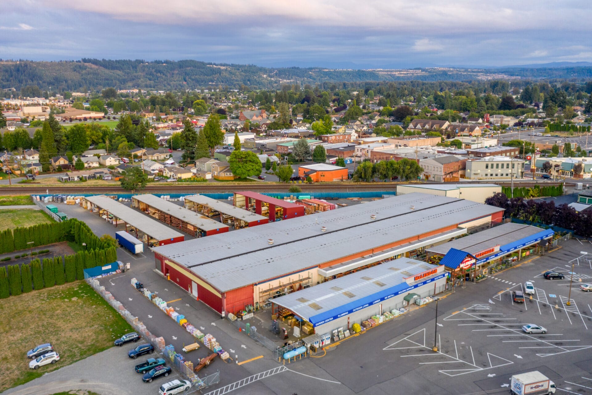 Aerial view of a large McLendon Hardware with a spacious parking lot, surrounded by various other buildings and greenery in a suburban area.