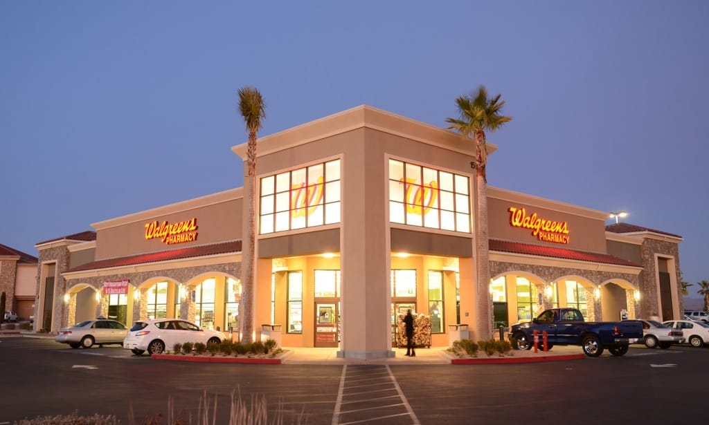 A Walgreens pharmacy store at twilight with illuminated signs, parked cars, and palm trees against a fading blue sky, showcasing a prime example of commercial real estate.