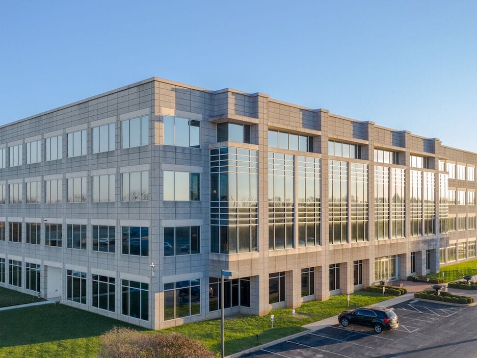 Modern office building with large glass windows on a sunny day, featuring parked cars and landscaped surroundings at Olympia Park.