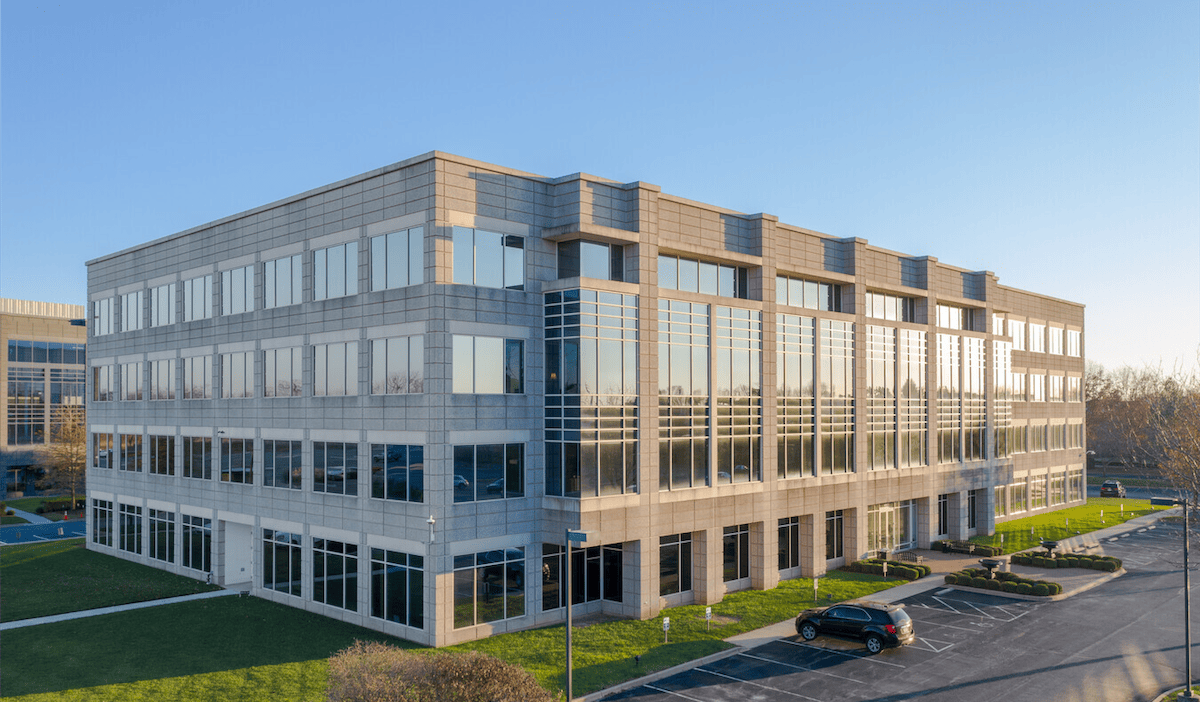 Modern office building with large glass windows on a sunny day, featuring parked cars and landscaped surroundings at Olympia Park.