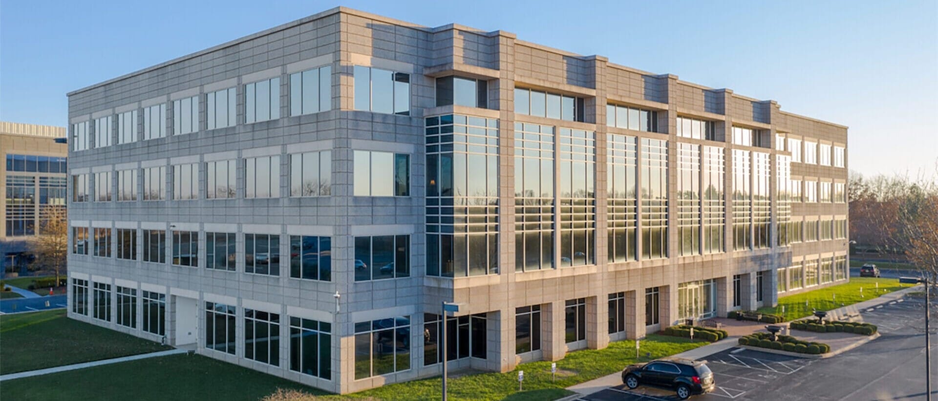 Modern three-story office building with large glass windows, surrounded by manicured lawns and a parking lot, under a clear blue sky, ideal for single tenant net leased investments nationwide.