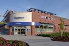 Exterior view of a Rite Aid pharmacy building with a drive-thru, landscaped with shrubs under a clear sky, positioned for single asset sales.