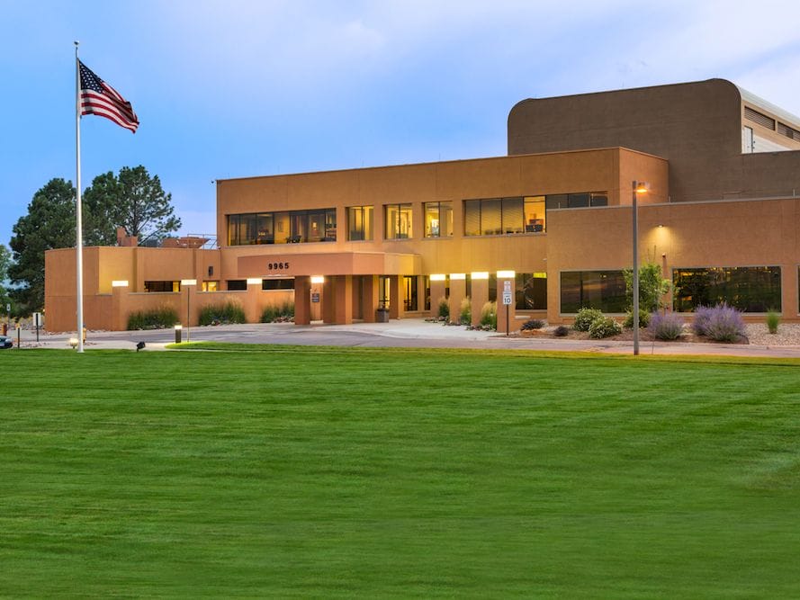 Modern office building with a Spectranetics flag flying in front, well-lit exterior, and landscaped surrounding during twilight.