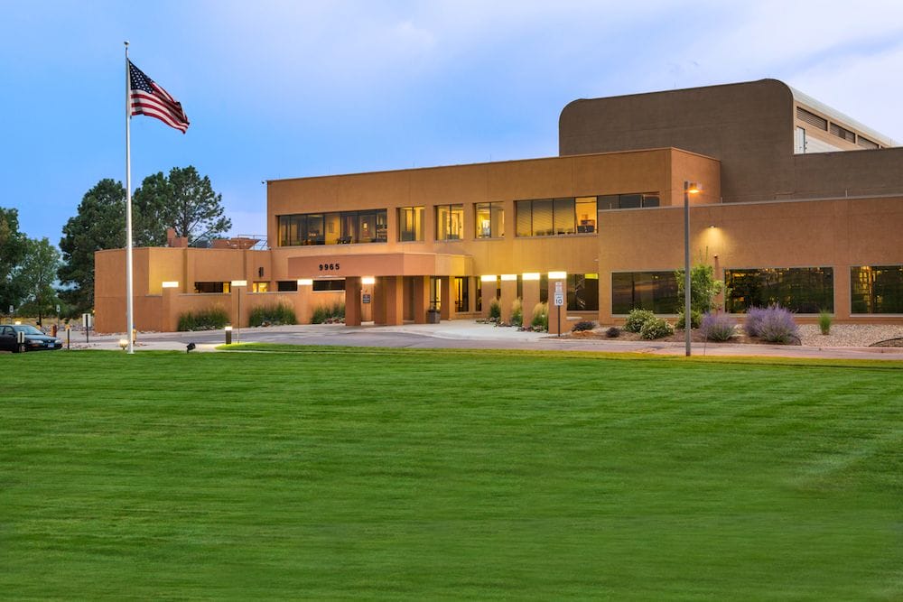 Modern office building with a Spectranetics flag flying in front, well-lit exterior, and landscaped surrounding during twilight.