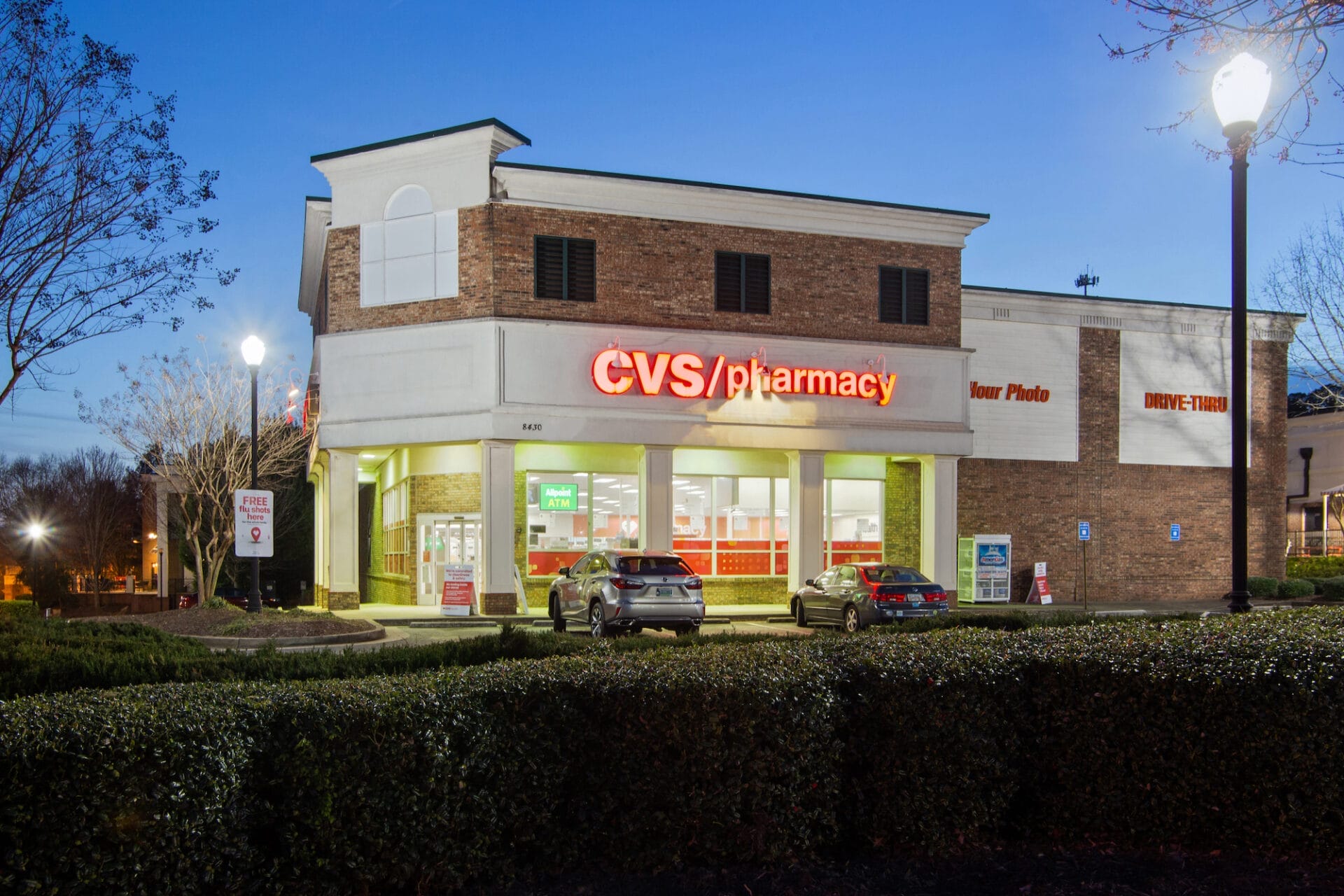 Exterior of a recently sold CVS Pharmacy store in Alpharetta, GA at twilight, illuminated by streetlights, with cars parked in front.