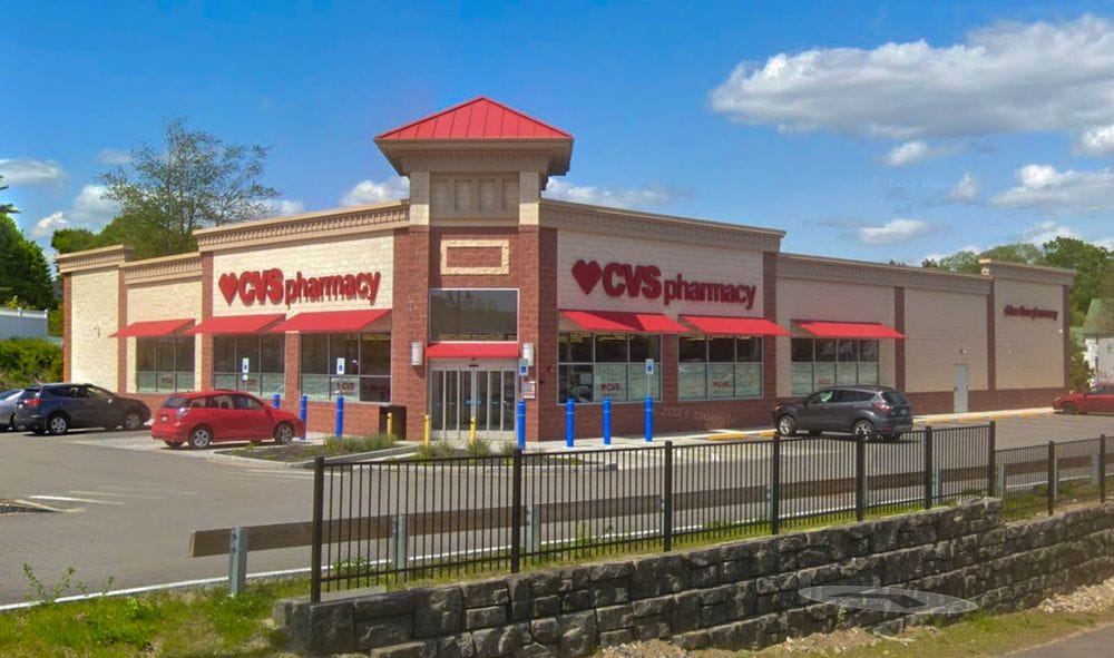 Exterior view of a CVS Pharmacy store advertising a sale with red signage, located in a one-story beige building under a clear blue sky.