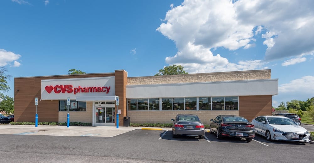 Exterior view of a recently sold CVS pharmacy store with a clear sky, featuring a parking lot with several cars.