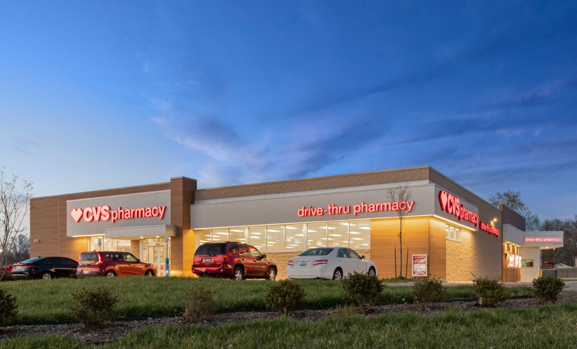 Exterior view of a recently sold CVS Pharmacy store in Louisville, Kentucky, at twilight with illuminated signage and cars parked outside.