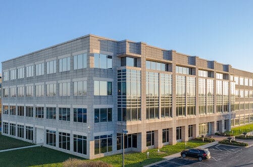 Modern multi-story Class-A office building in Louisville, Kentucky, with large glass windows, surrounded by a manicured lawn under a clear blue sky.