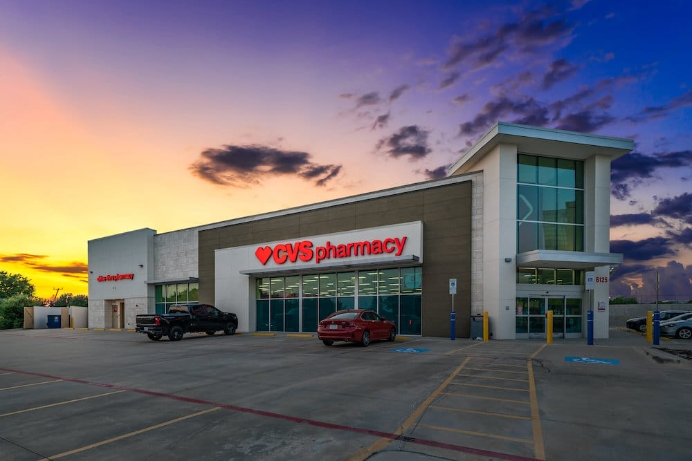 Exterior view of a recently sold CVS pharmacy store in Plano, Texas at sunset with vibrant sky colors, featuring a parking lot with a few cars.