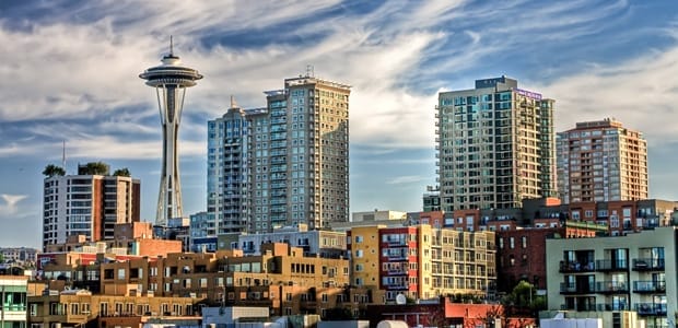 Seattle skyline featuring the Space Needle, various modern buildings under a cloudy sky, and the prominent Thomas Company building.