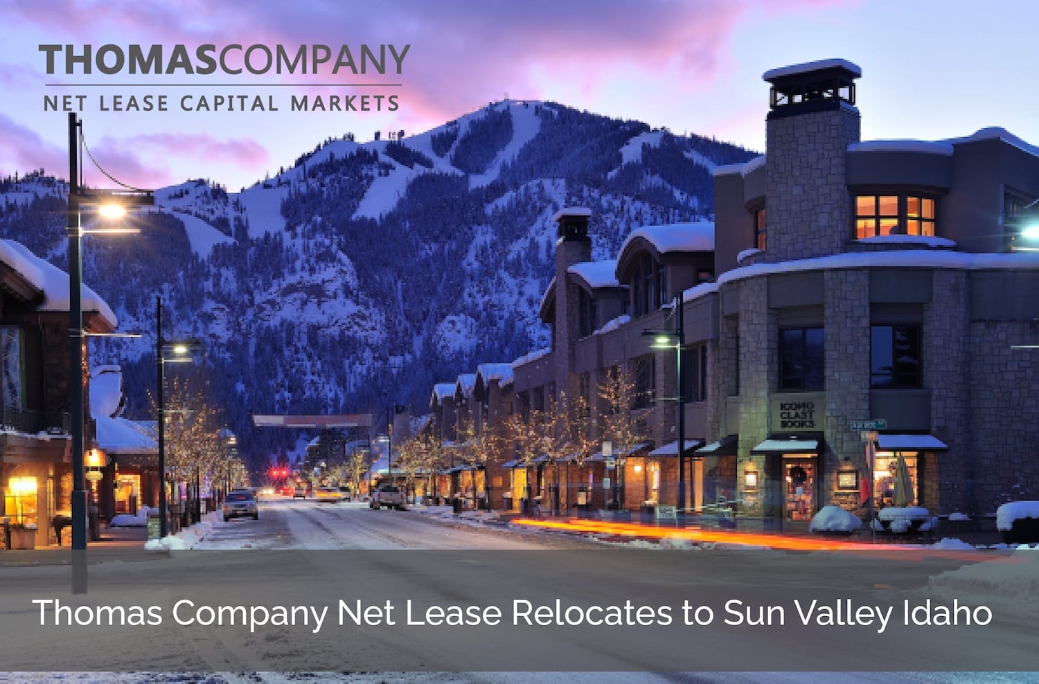 Sunset view of Sun Valley, Idaho, with snow-covered mountains in the background and lit-up street and buildings in the foreground, featuring the Thomas Company logo and announcement text about their relocation to Sun Valley