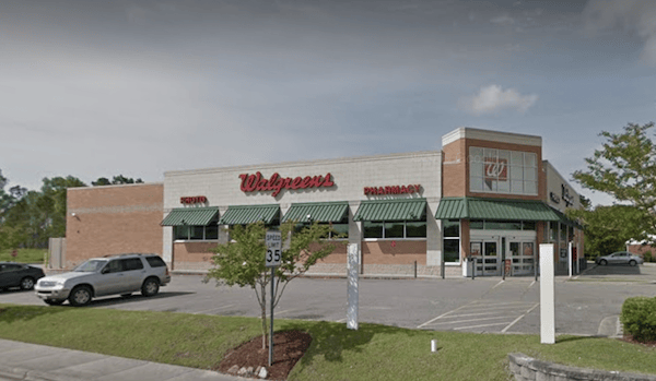 Exterior view of a recently sold Walgreens store in Shallotte NC with a visible pharmacy sign, parked cars, trees, and clear skies.