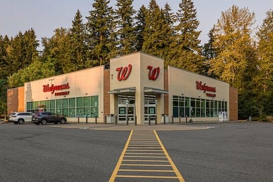 Exterior view of the recently sold Walgreens Woodinville store with a large parking area, surrounded by trees, under a clear sky.