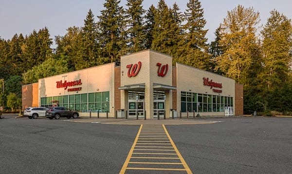 Exterior view of the recently sold Walgreens Woodinville store with a large parking area, surrounded by trees, under a clear sky.