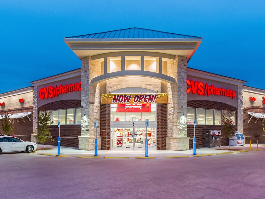 Exterior view of a CVS Pharmacy store illuminated at twilight, featuring prominent signage, parked cars, and a clear sky. This single tenant net leased property highlights the appeal of such investments nationwide.