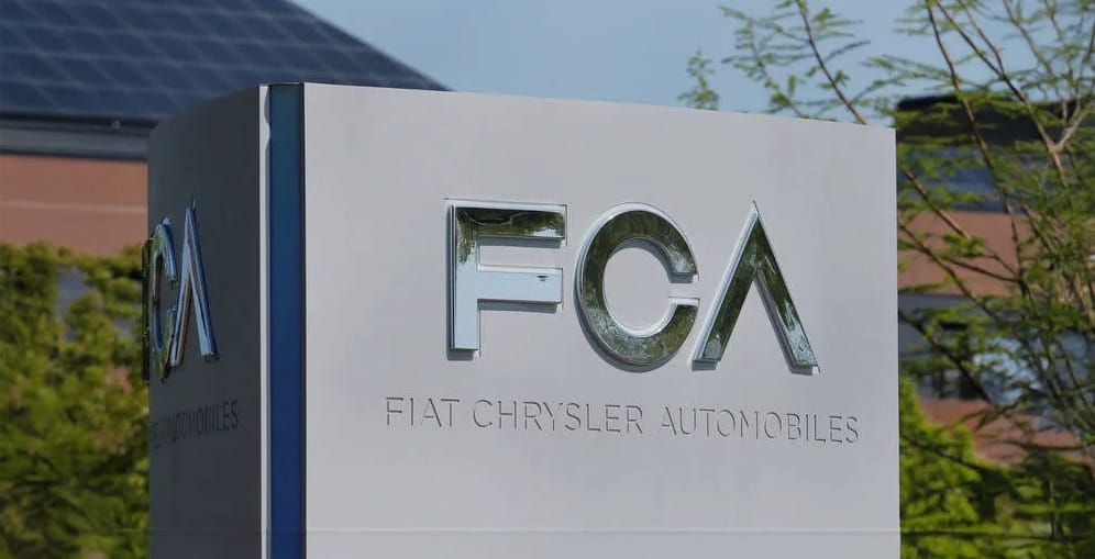 A sign displaying the FCA logo with the text "Fiat Chrysler Automobiles" stands outdoors near a building and foliage, marking the site of a recently sold distribution center.