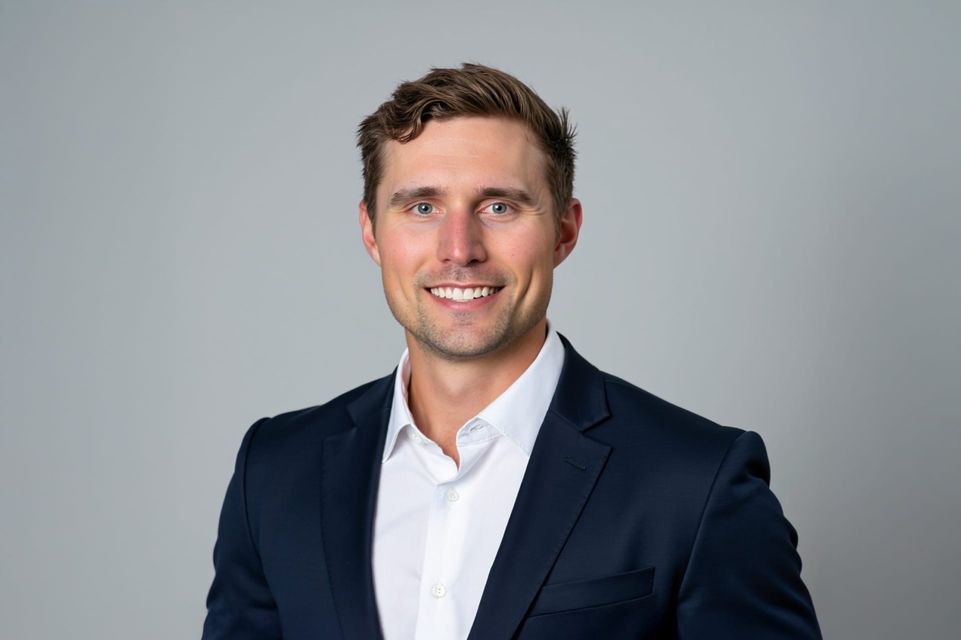 Brian Steck, dressed in a navy suit and white shirt, smiles at the camera against a plain light gray background.